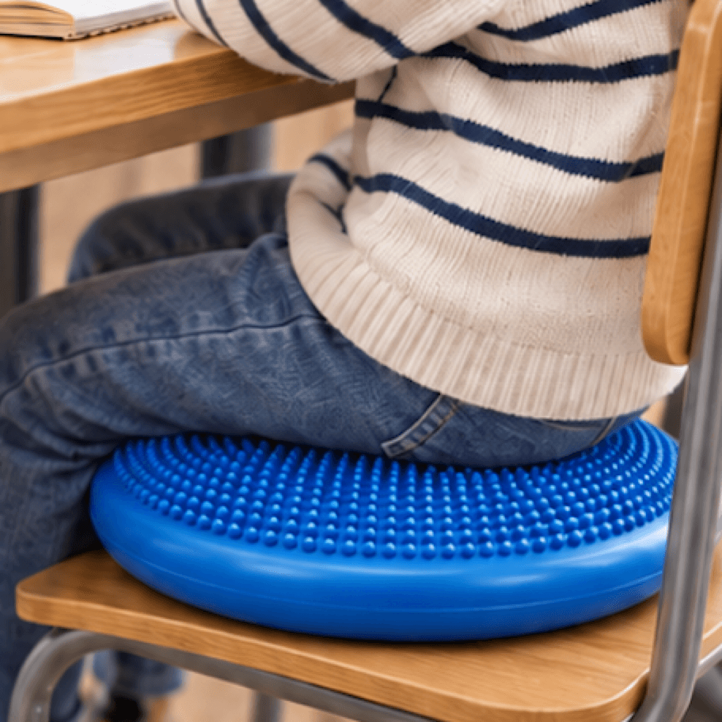 Niño sentado sobre un cojín sensorial azul en una silla escolar